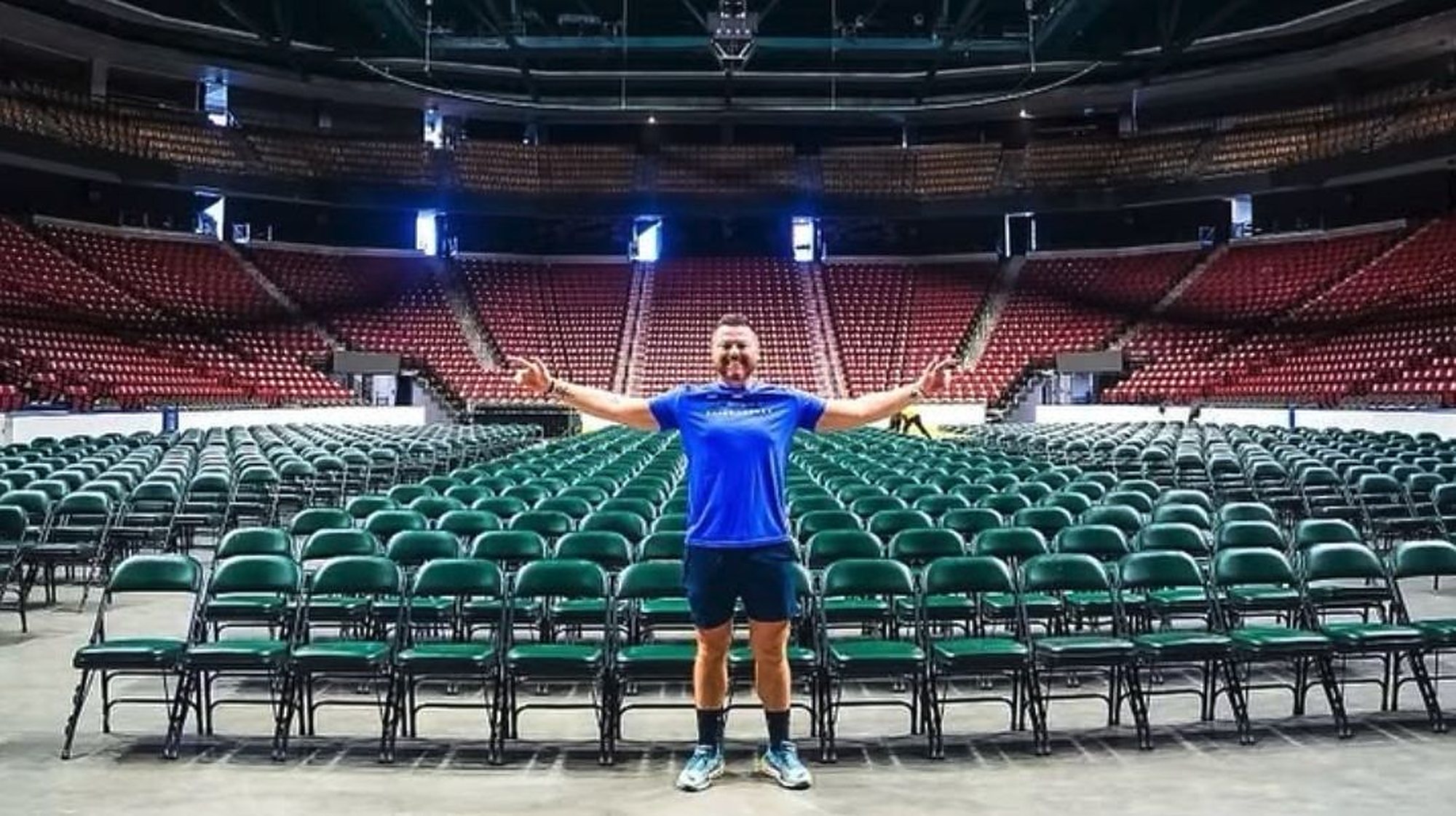 Brian Rand standing in an empty arena with rows of chairs behind him